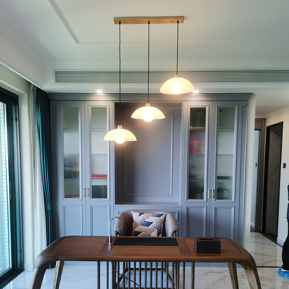 Three alabaster pendants from Clérachic on one long brass canopy, hanging at staggered heights above a wooden desk in a study.