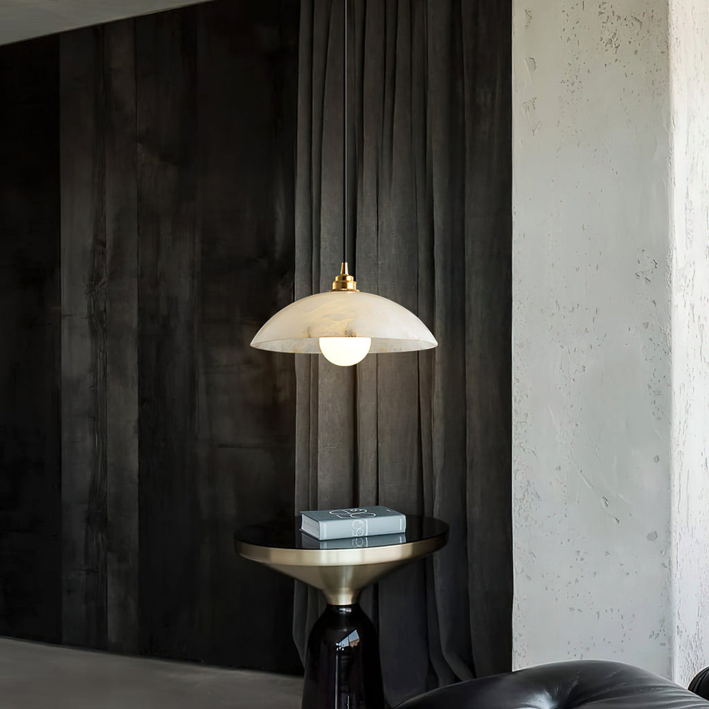 Alabaster dome pendant from Clérachic lit against dark curtains and a rough concrete wall, with a brass side table below.
