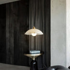 Alabaster dome pendant from Clérachic lit against dark curtains and a rough concrete wall, with a brass side table below.