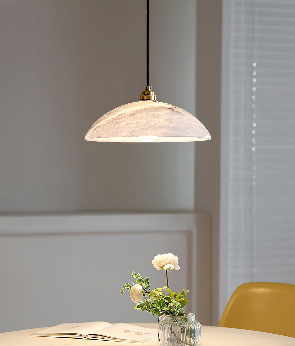Pale marbled dome of this Clérachic pendant seen near a window with blinds, above a table with an open book and a small rose in a vase.