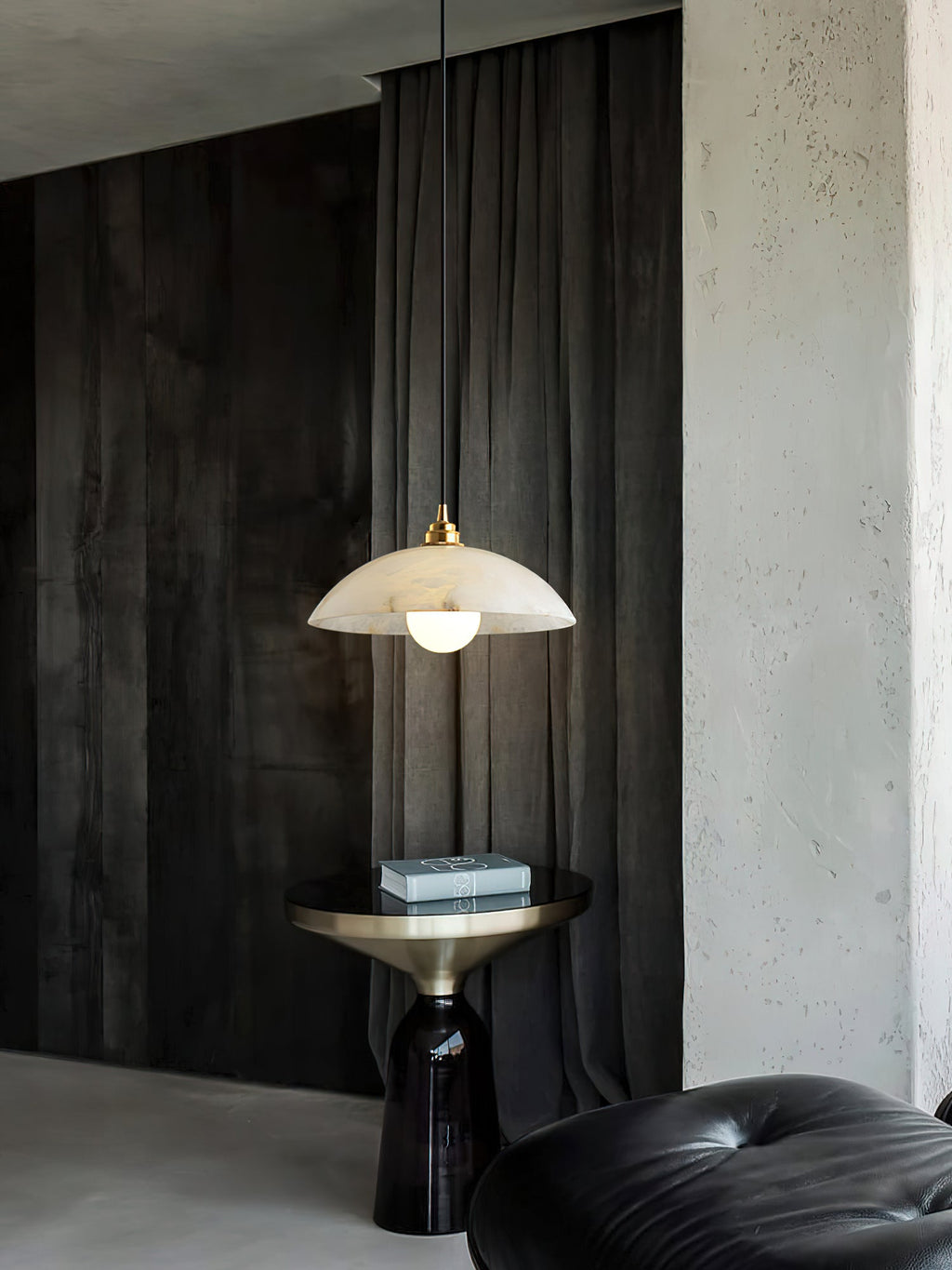 This Clérachic pendant hung in front of grey-black drapes, its dome lit warm, with a brass side table and a black leather pouffe below.