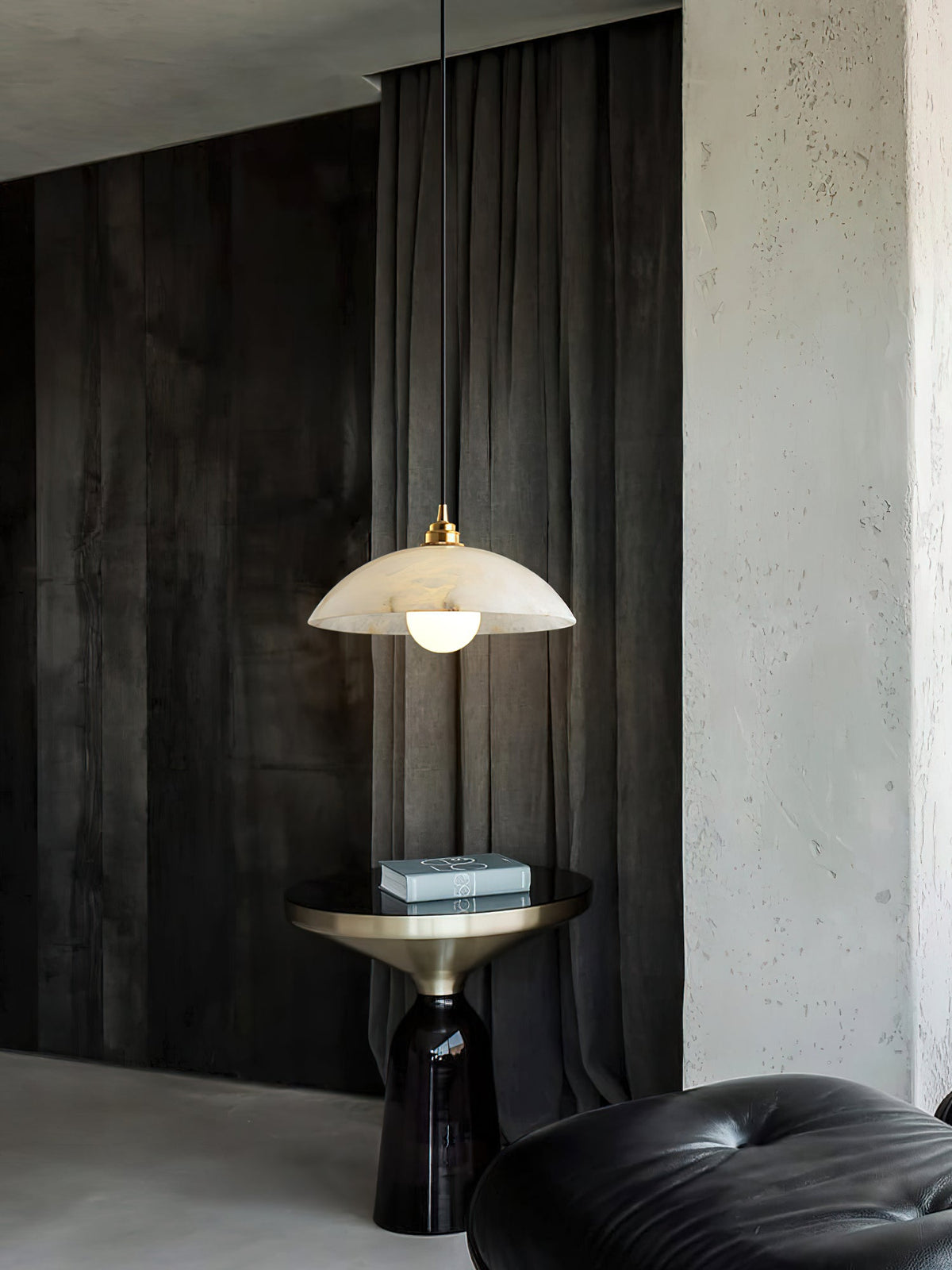 This Clérachic pendant hung in front of grey-black drapes, its dome lit warm, with a brass side table and a black leather pouffe below.