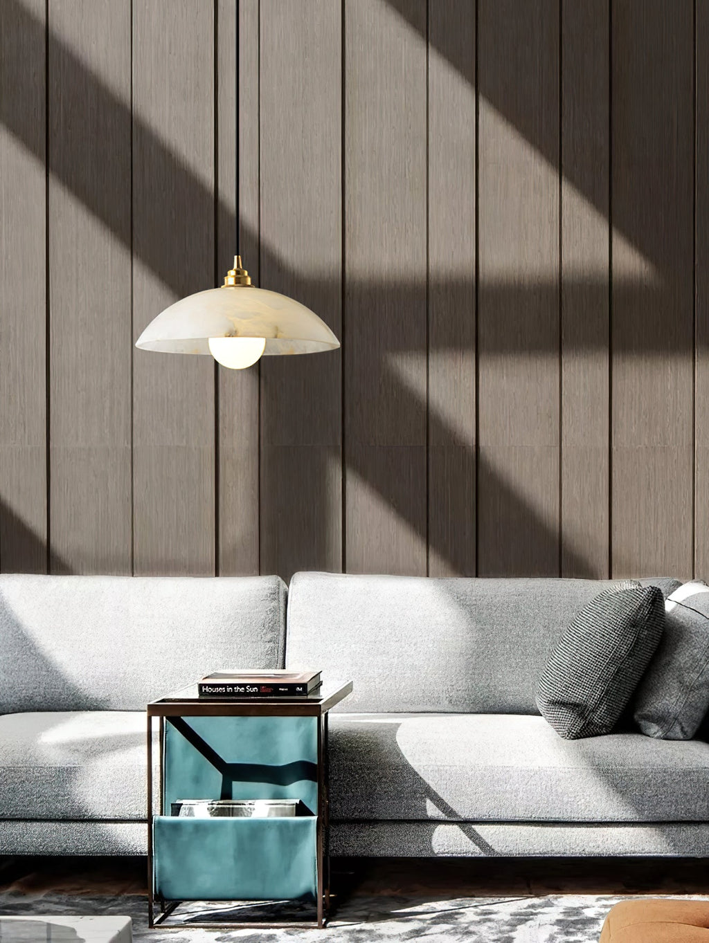A Clérachic pendant hung over a grey sofa and a teal side table, with sunlight casting shadows across a wall of vertical wooden slats.