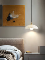 Lit Clérachic alabaster pendant beside a bed with a taupe headboard, a bedside table and a mustard abstract painting behind.