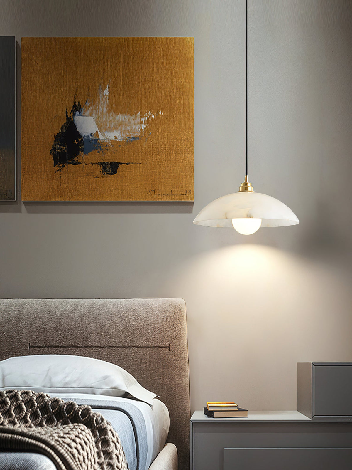 Lit Clérachic alabaster pendant beside a bed with a taupe headboard, a bedside table and a mustard abstract painting behind.