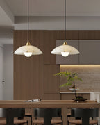 Two Clérachic pendants with white alabaster domes hanging above a wooden counter with bar stools, in front of a warm timber kitchen wall.