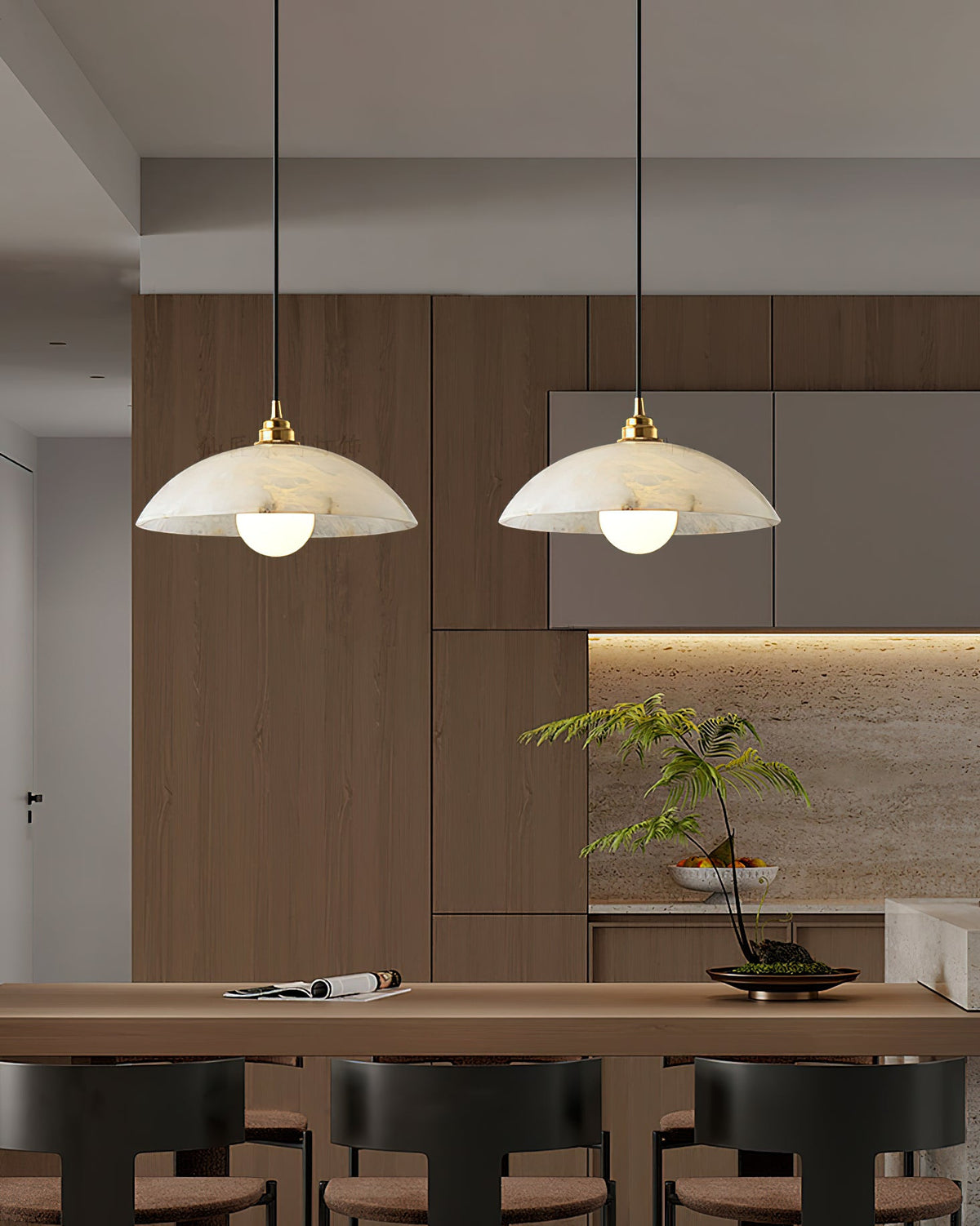 Two Clérachic pendants with white alabaster domes hanging above a wooden counter with bar stools, in front of a warm timber kitchen wall.