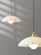 Two alabaster domes of this Clérachic pendant at different heights, in cropped close view against a grey wall striped with sunlight.