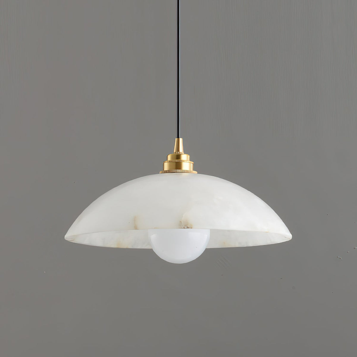 Close side view of a Clérachic alabaster pendant, showing the stepped brass lamp holder and a round opal bulb below the rim.