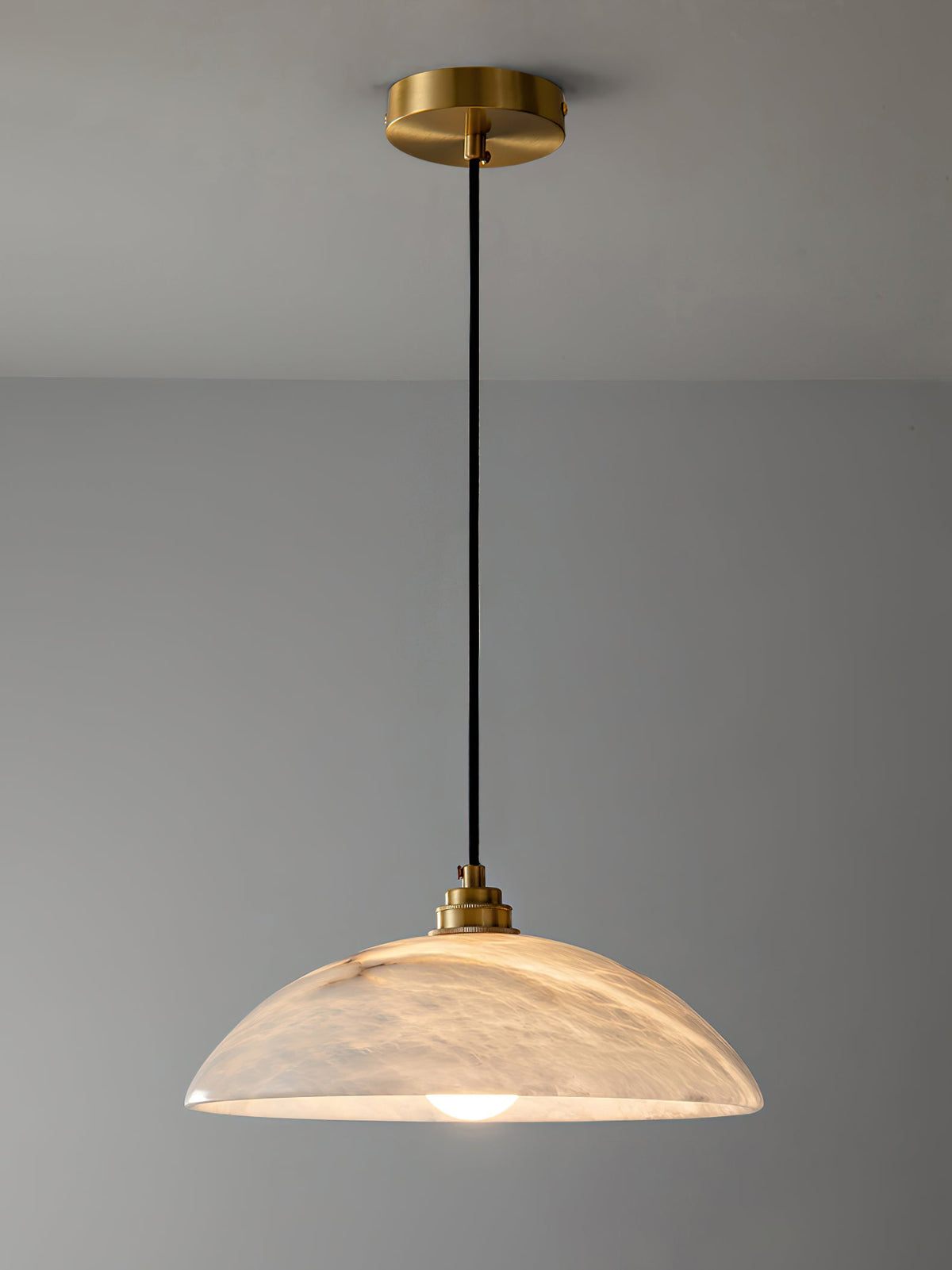 Full drop of this Clérachic pendant, from a round brass ceiling plate down a black cord to a lit, veined alabaster dome.