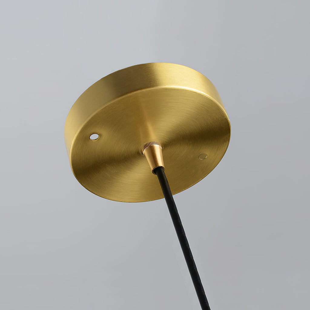 Close view of the round brushed-brass ceiling plate and black cord at the top of this Clérachic pendant.