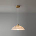 Clérachic alabaster pendant hung from a brass ceiling plate against a grey wall, its dome lit warm with faint peach veining.