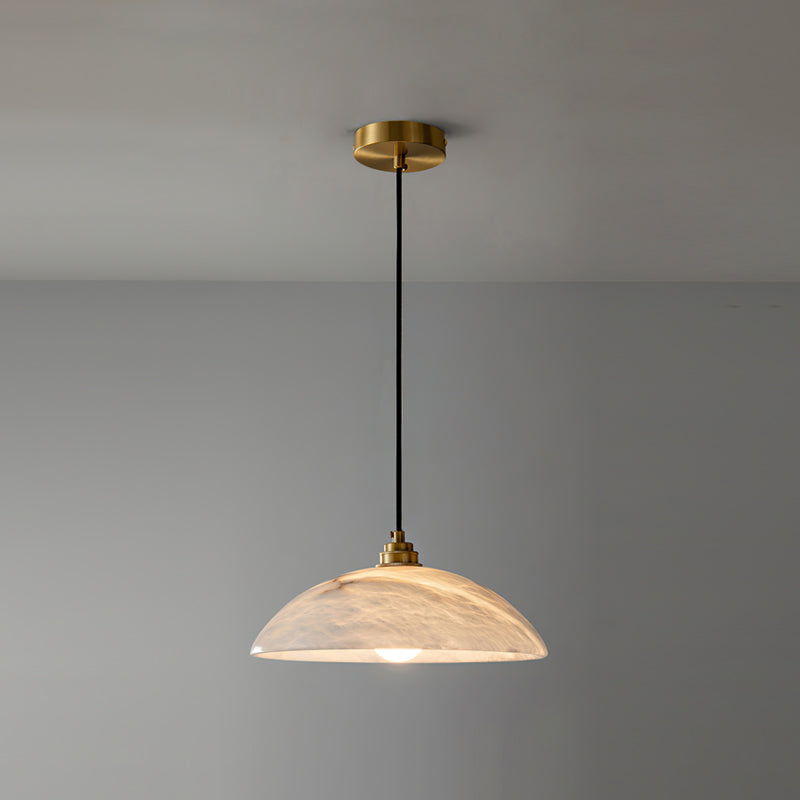 Clérachic alabaster pendant hung from a brass ceiling plate against a grey wall, its dome lit warm with faint peach veining.