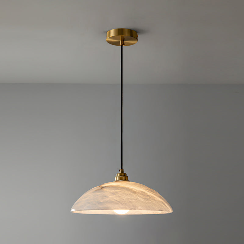 A slightly larger view of this Clérachic pendant, with the brass ceiling plate, black cord and warm-lit alabaster dome against a grey wall.