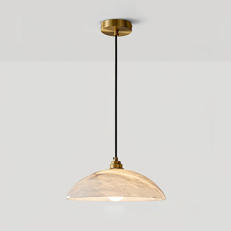 Clérachic alabaster pendant hung on a long black cord from its brass ceiling plate, lit warm, against a light grey wall.