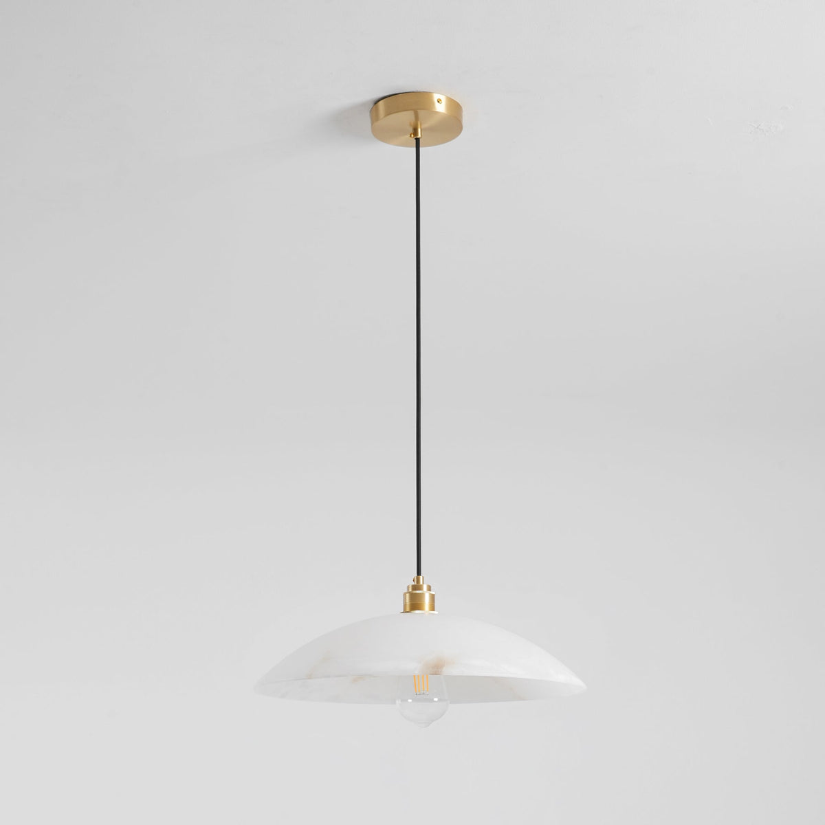 Unlit Clérachic pendant with a milky white alabaster dome and a clear bulb, hanging from a brass ceiling plate against a white wall.