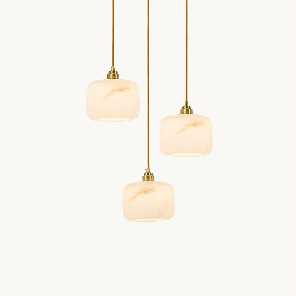Three alabaster Clérachic pendants with brass hardware hung at different heights on a plain off-white backdrop.