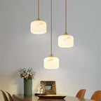 A trio of Clérachic alabaster pendants on brass rods above a dark wood table, with a vase of flowers and framed art below.