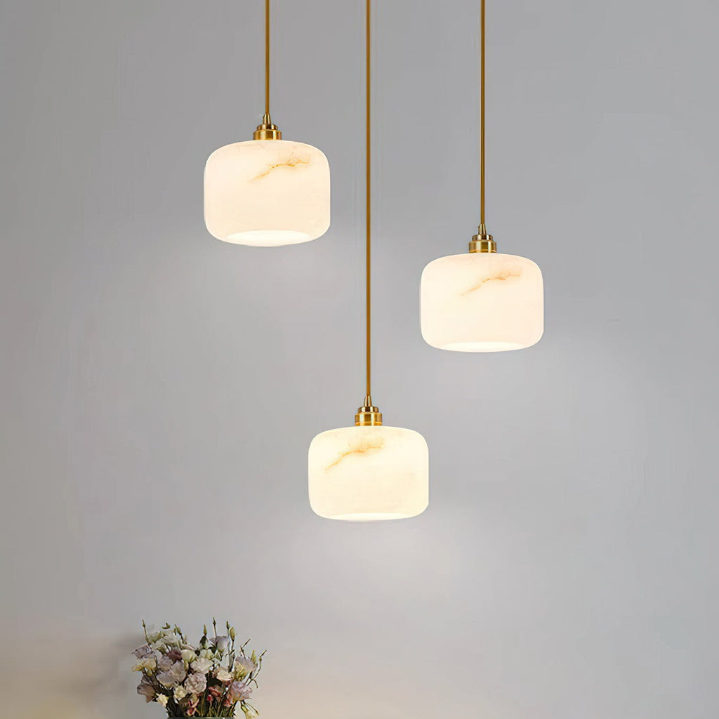 Three Clérachic alabaster pendants hung at staggered heights against a pale grey wall, the veining warm gold under the light.