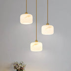 Three Clérachic alabaster pendants hung at staggered heights against a pale grey wall, the veining warm gold under the light.