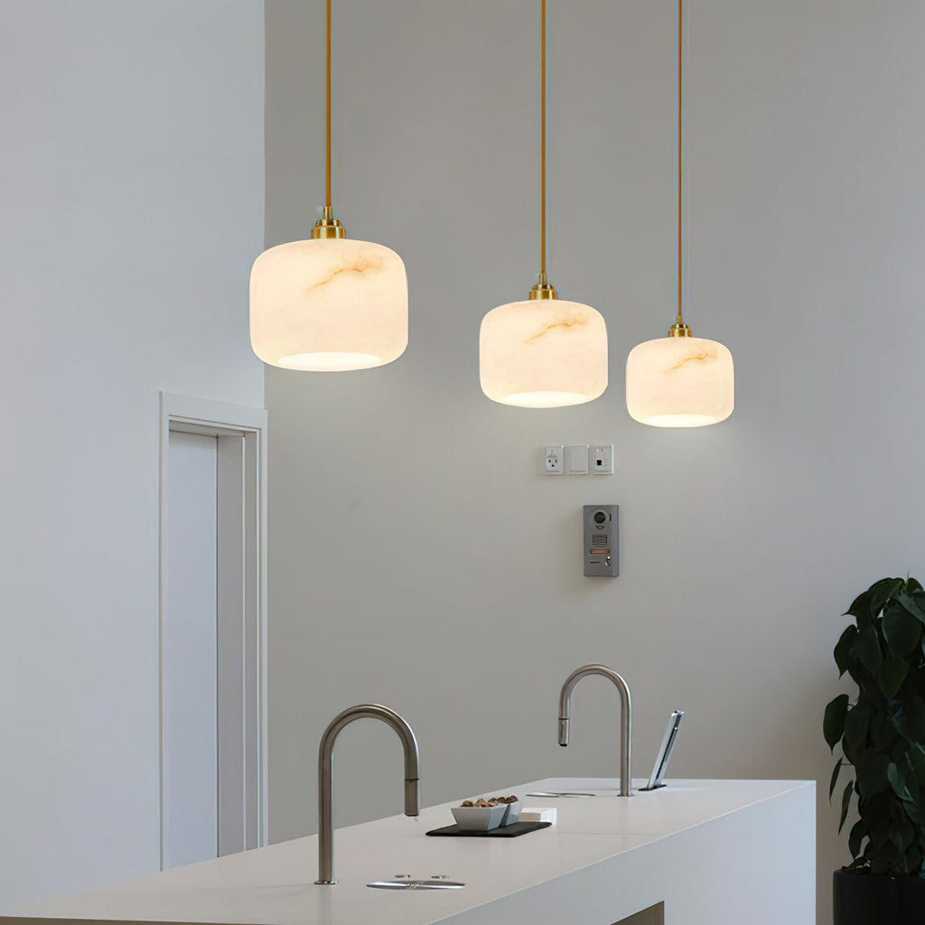 Wide kitchen view of three graduated alabaster pendants from Clérachic, above a white counter with two brushed-steel taps.