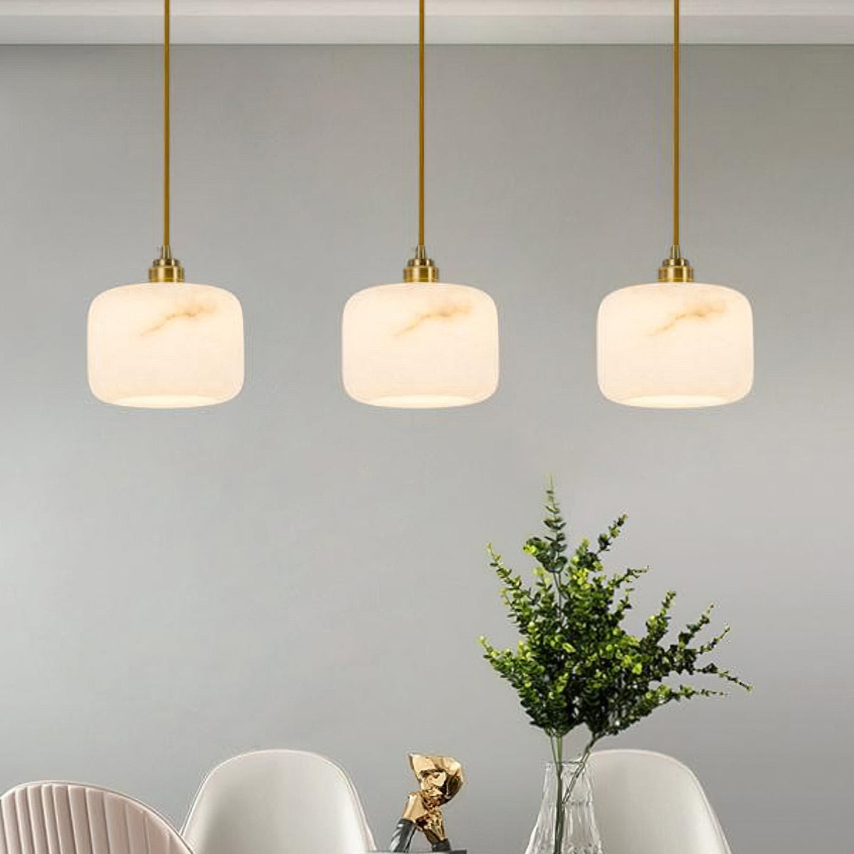 Three matching Clérachic pendants in a row above a dining table, with white shell chairs and a green plant below.