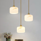 Three alabaster Clérachic pendants glowing at staggered heights, with a vase of pale flowers at the bottom of the frame.