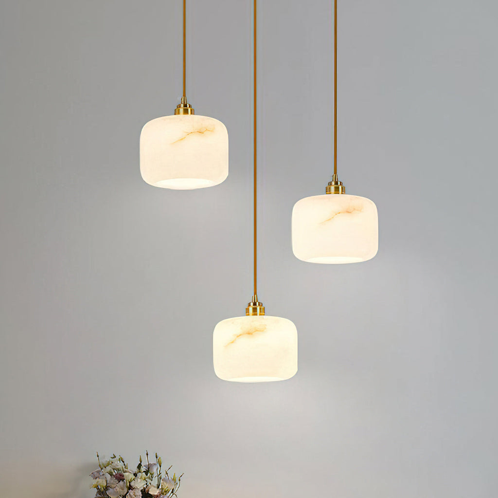 Close grouping of three Clérachic pendants with cream alabaster shades, their gold-toned veining lit softly from inside.