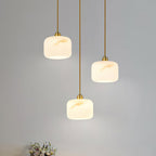 Close grouping of three Clérachic pendants with cream alabaster shades, their gold-toned veining lit softly from inside.