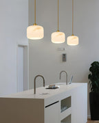 Tall kitchen with three alabaster Clérachic pendants glowing above a white island, with a dark plant in the corner.