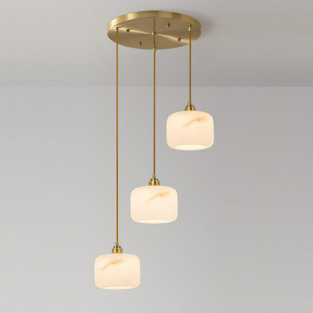Three Clérachic alabaster pendants of different heights hanging from one round brass canopy, shown against a grey wall.