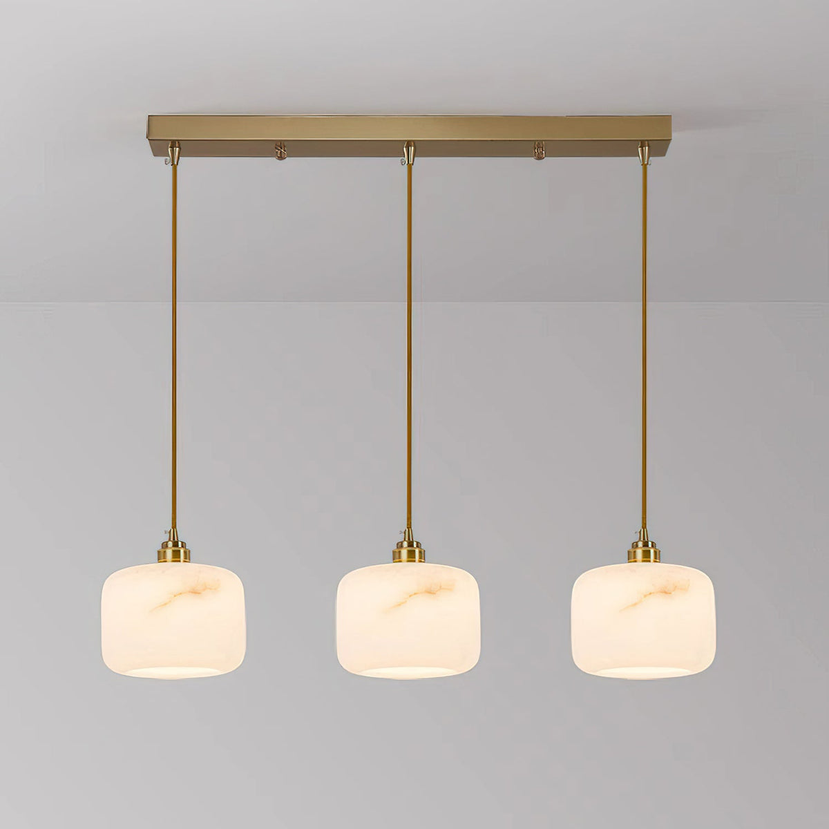 Three alabaster Clérachic pendants lit in a row from a long rectangular brass bar, with matching brass rods.