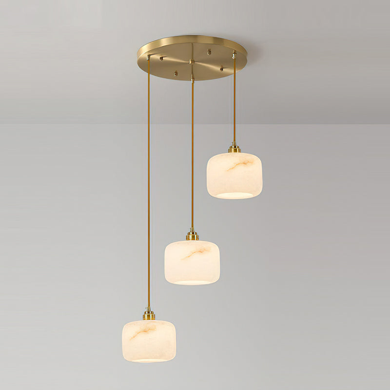 Three Clérachic alabaster pendants cascading at different heights from a round brass ceiling plate, glowing warmly.