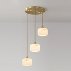 Three Clérachic alabaster pendants cascading at different heights from a round brass ceiling plate, glowing warmly.