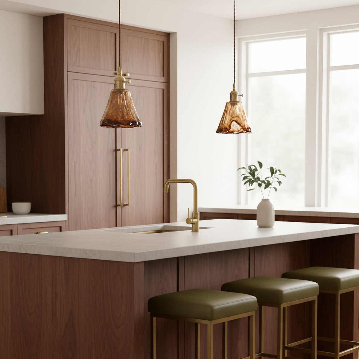 Two Clérachic amber glass pendants over a walnut kitchen island with olive-green stools and a brass tap.