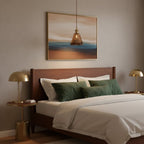 This Clérachic amber pendant hangs above a bed with green cushions, in front of a framed seascape and between two brass bedside lamps.