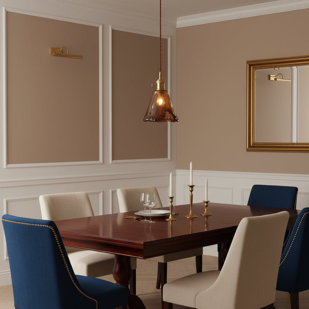 A Clérachic amber glass pendant hangs above a dark wood dining table with blue chairs, candlesticks and a gilt mirror behind.