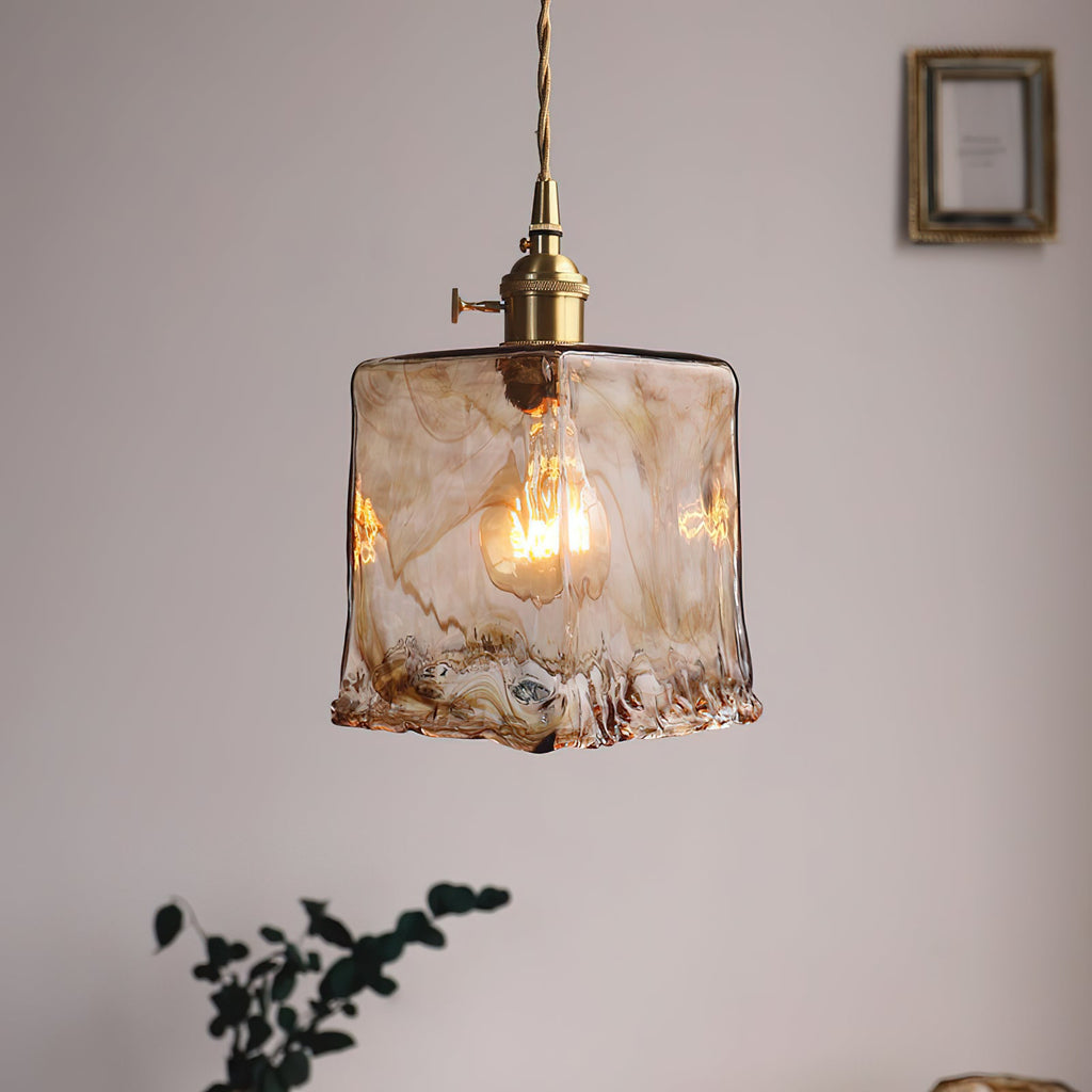 Clérachic pendant with a squared amber glass shade and a visible bulb, hanging by a framed picture, with a plant below.