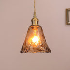 Clérachic pendant with a flared amber glass shade, lit, with its brass cap and a twisted cord, against a dusty-pink wall.