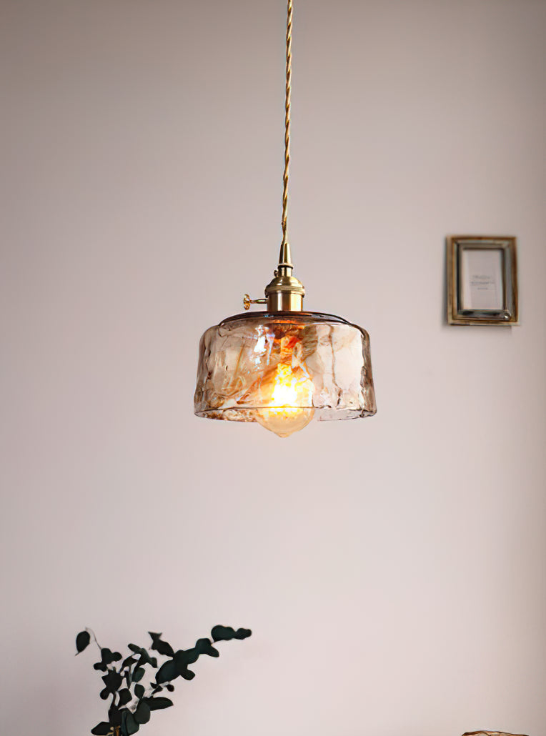 Clérachic pendant with a low, round amber glass shade, seen from a distance with a plant and a small frame nearby.