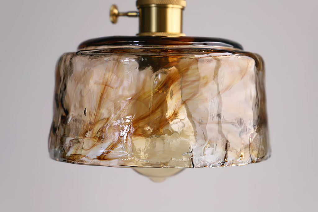 Close view of the marbled amber glass on a low, round Clérachic pendant, with the globe bulb just visible below.