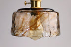 Close view of the marbled amber glass on a low, round Clérachic pendant, with the globe bulb just visible below.