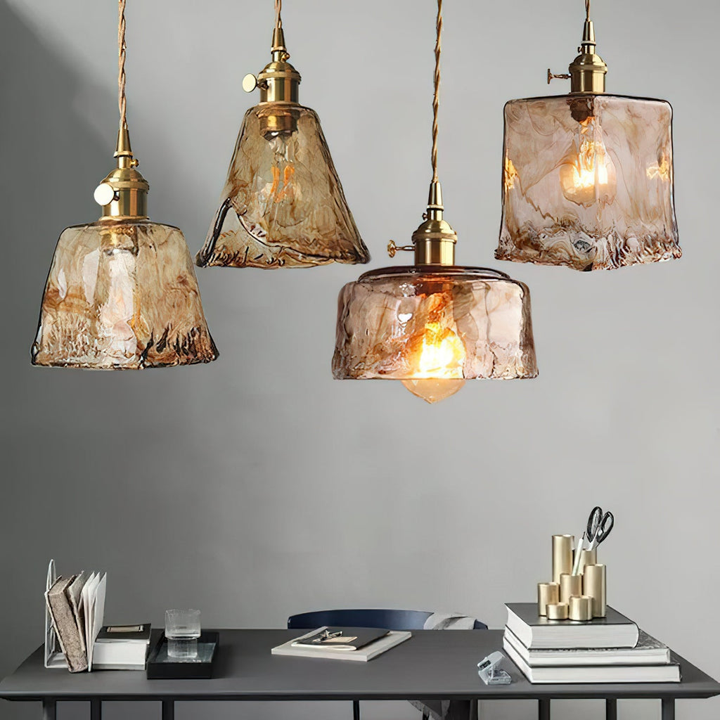 Four Clérachic amber glass pendants hanging at different heights above a dark desk with books, with a grey wall behind.