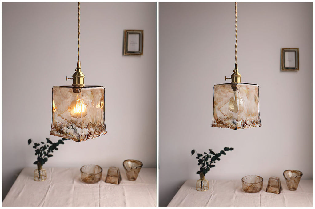 Two views side by side, with a Clérachic squared amber glass pendant lit at left and unlit at right, above a table with glass pieces.