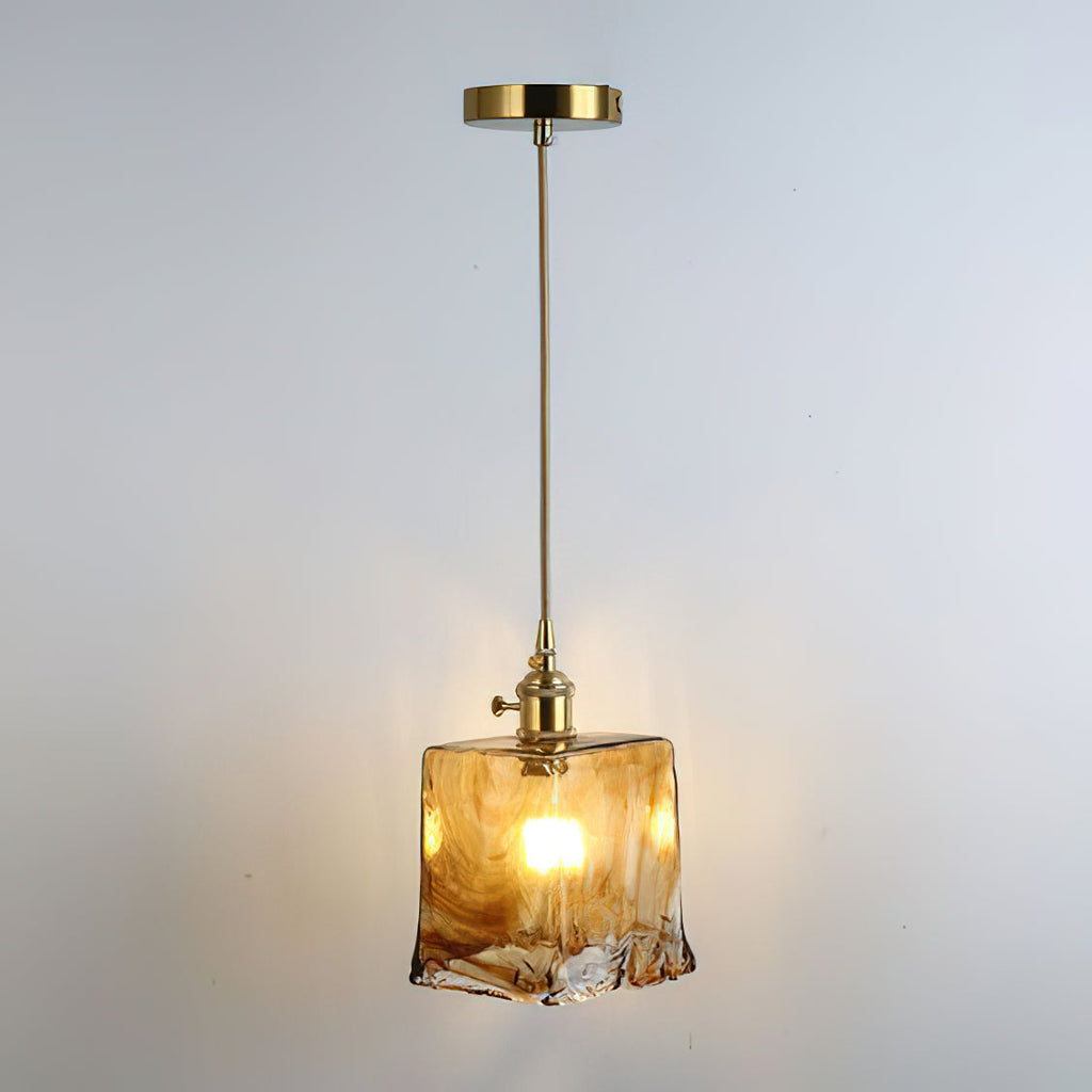 Clérachic pendant with a squared amber glass shade, lit, hanging from a brass ceiling plate and a thin brass rod.