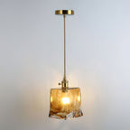 Clérachic pendant with a squared amber glass shade, lit, hanging from a brass ceiling plate and a thin brass rod.