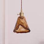 A Clérachic pendant with a flared amber glass shade and a darker fused edge, unlit, on a plain pale wall.