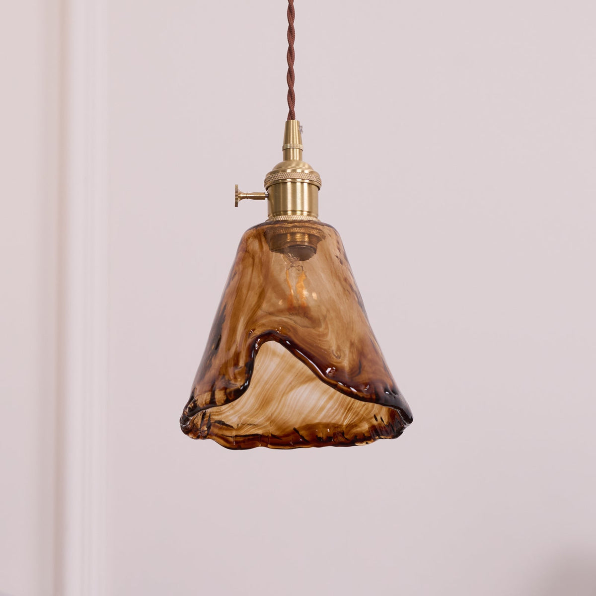 A Clérachic pendant with a flared amber glass shade and a darker fused edge, unlit, on a plain pale wall.