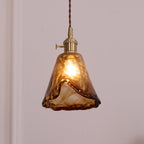 Clérachic pendant with a flared amber glass shade, lit, showing deep brown swirls near the hem and a brass switch holder.