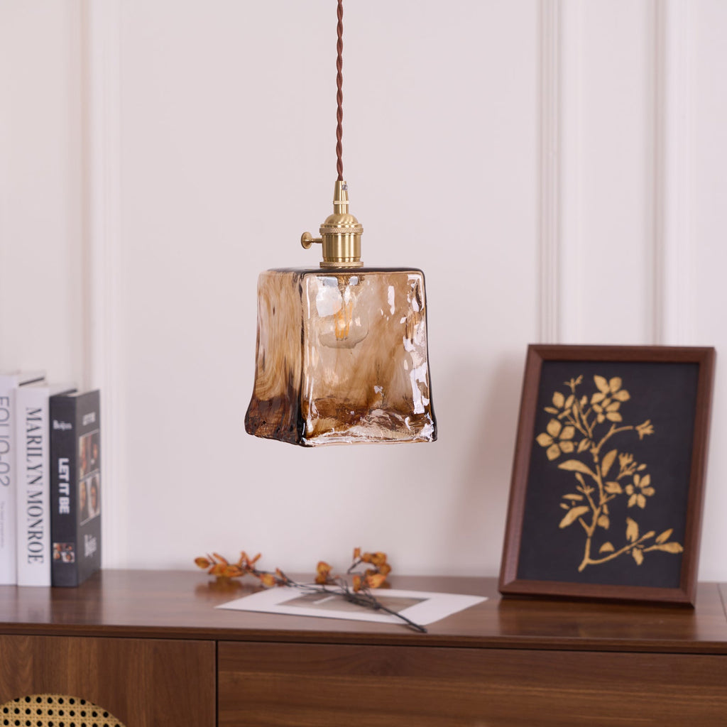 Clérachic pendant with a squared amber glass shade, unlit, hanging above a console with a gold-on-black framed print and books.